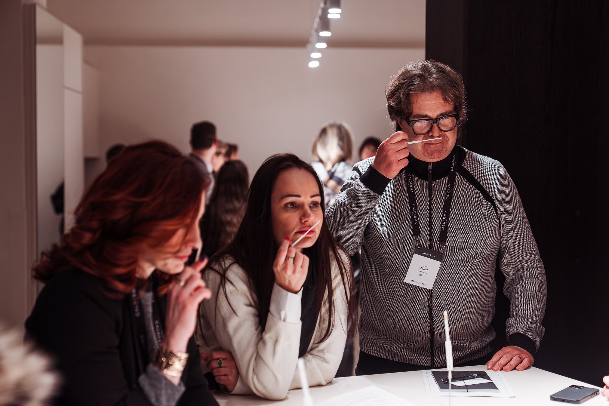 Event photography Vienna.People smelling candles at a conference or exhibition, with a man in glasses and a woman with long dark hair in focus.
