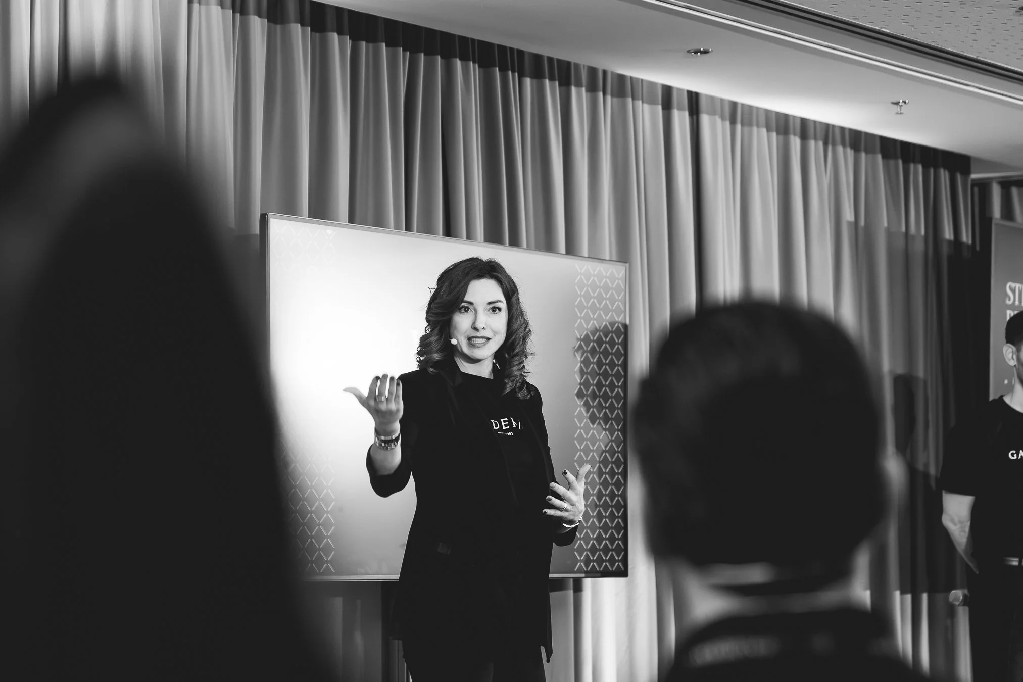 A woman with wavy hair giving a presentation in front of a screen with an audience in a conference room. Galderma Event Vienna