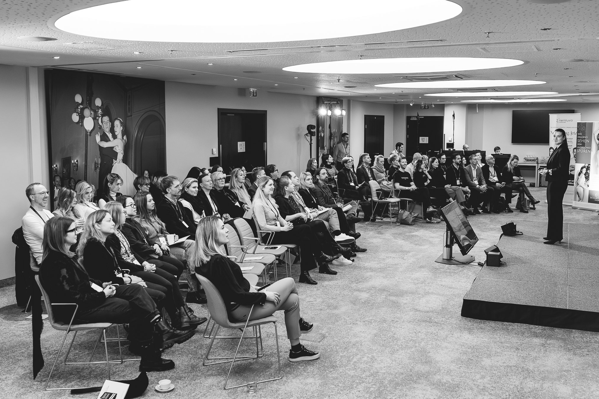 Event Photography Vienna.A woman giving a presentation to an audience in a conference room, with attendees seated and listening attentively.