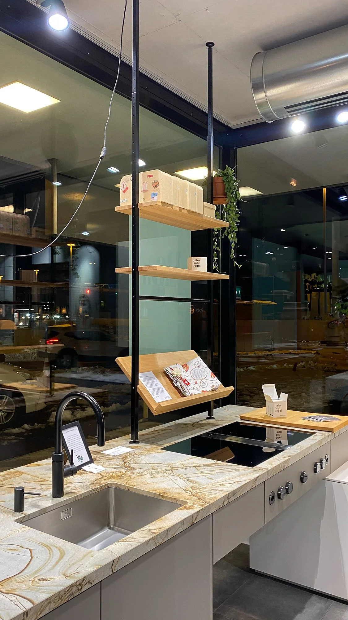 Küche von Baumann Küchen, darunter Herd und Spüle, auf der Küchenarmatur befindet sich eingeklemmt das Johann's Teleskoregal mit Magazinablage Pflanzenständer und Küchenutensilien.