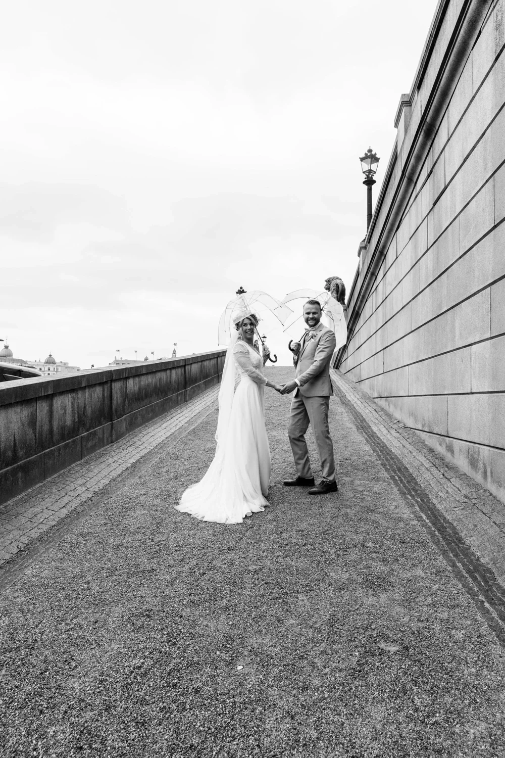 Anna och Martin i helfigur vid en stenmur, svartvitt bröllopsporträtt.