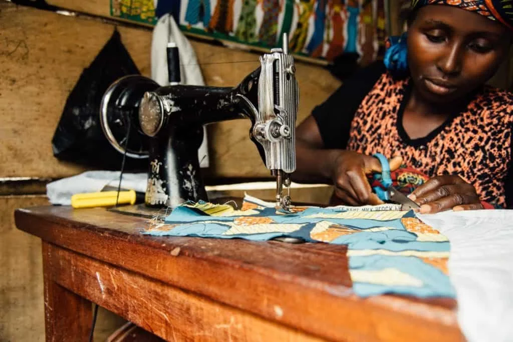 A woman using a sewing machine to stitch fabric in a workshop.