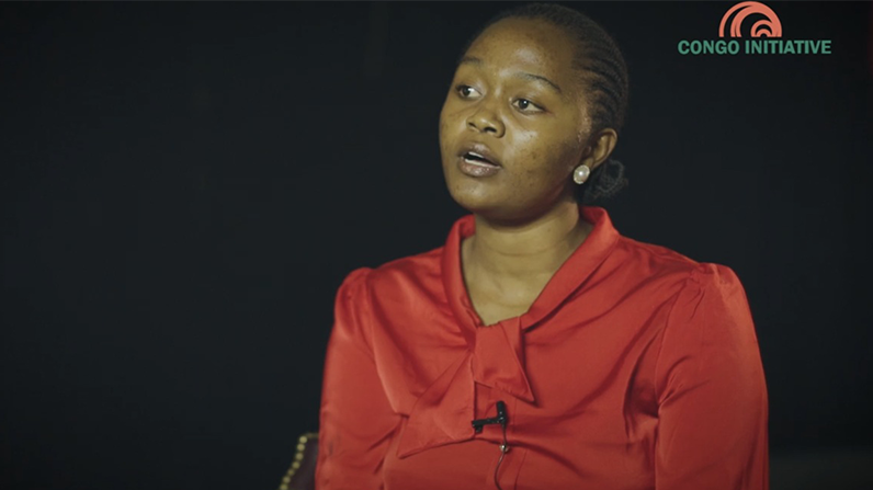 A woman wearing a red blouse is speaking in a video interview against a black background. The logo 'Congo Initiative' is visible in the top right corner.