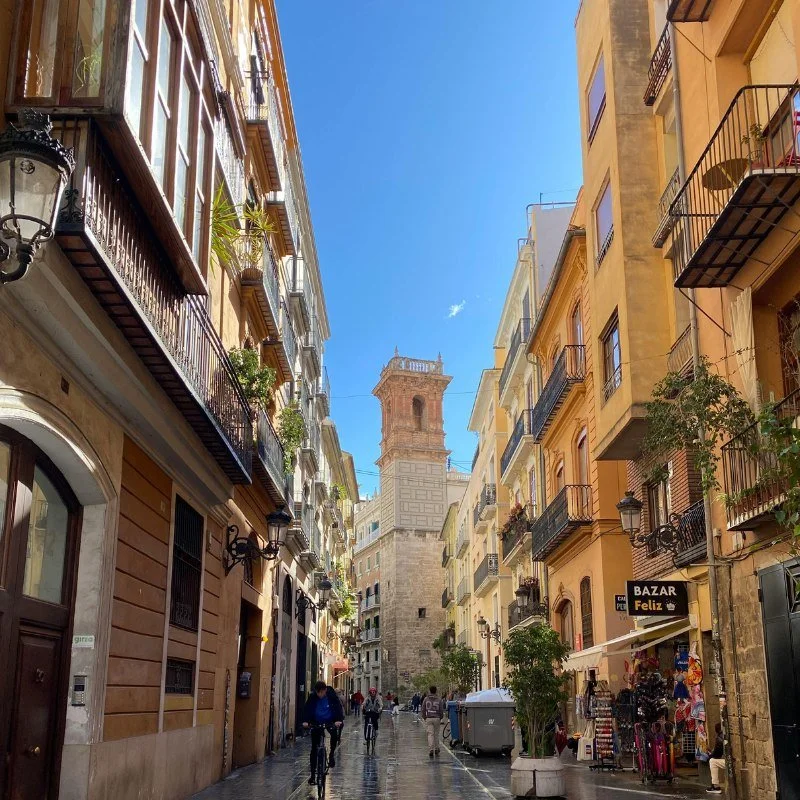 a narrow street with a view of the Miguelete bell tower.