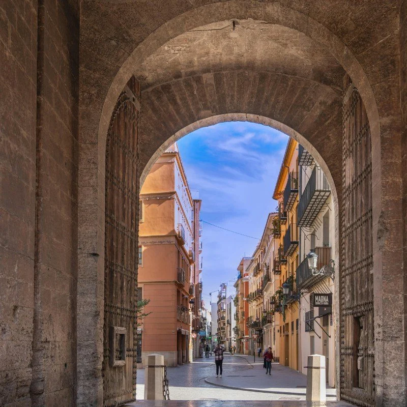 a view down a bright Valencian street through a large historic archway.