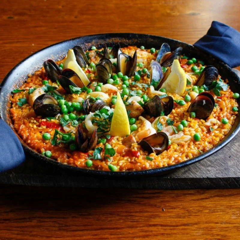 a seafood paella, topped with muscles, peas and lemon