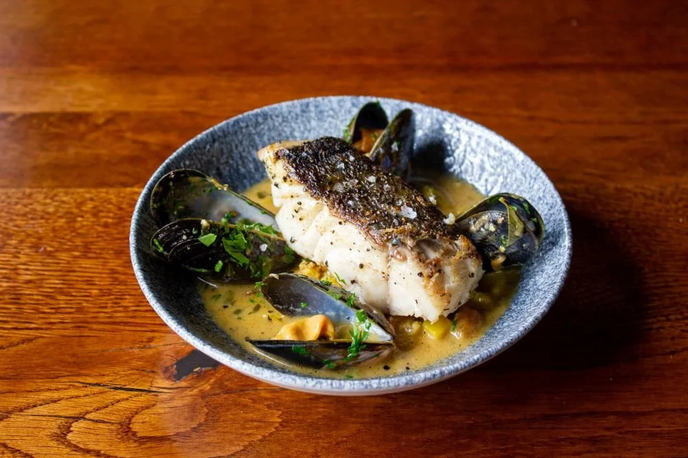 A bowl of Fish Stew topped with crispy fish and mussels
