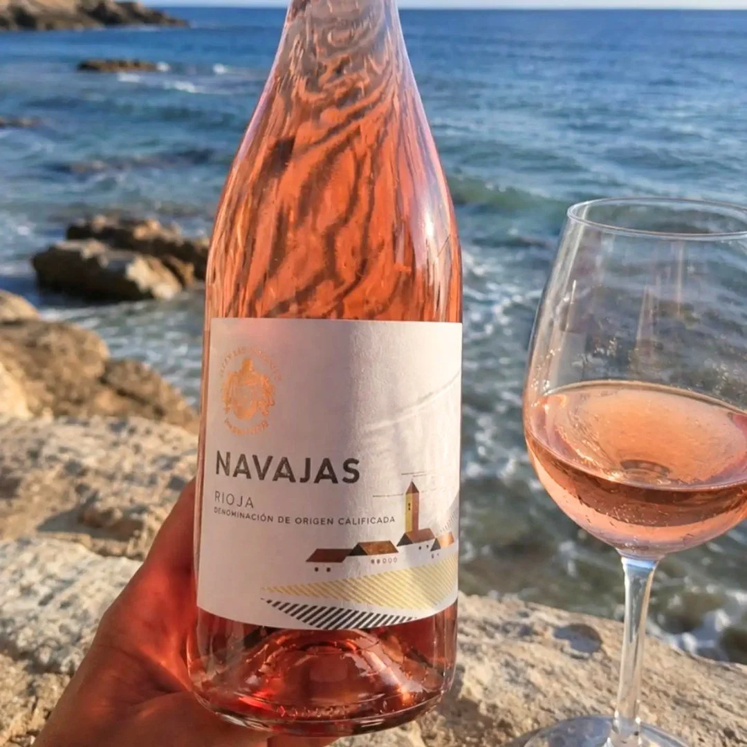 Bottle of Rose wine next to a poured glass with the beach in the background.