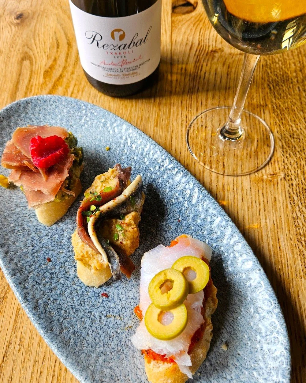 Side image of three pintxos and bottle of txakoli with glass of wine