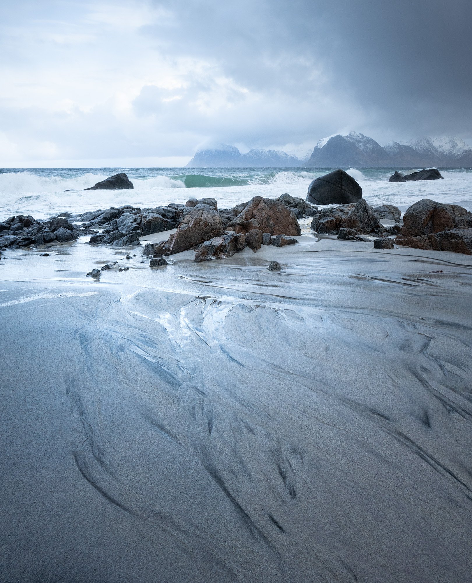 Rocky beach in Lofoten with wet sand and ocean waves under stormy sky.