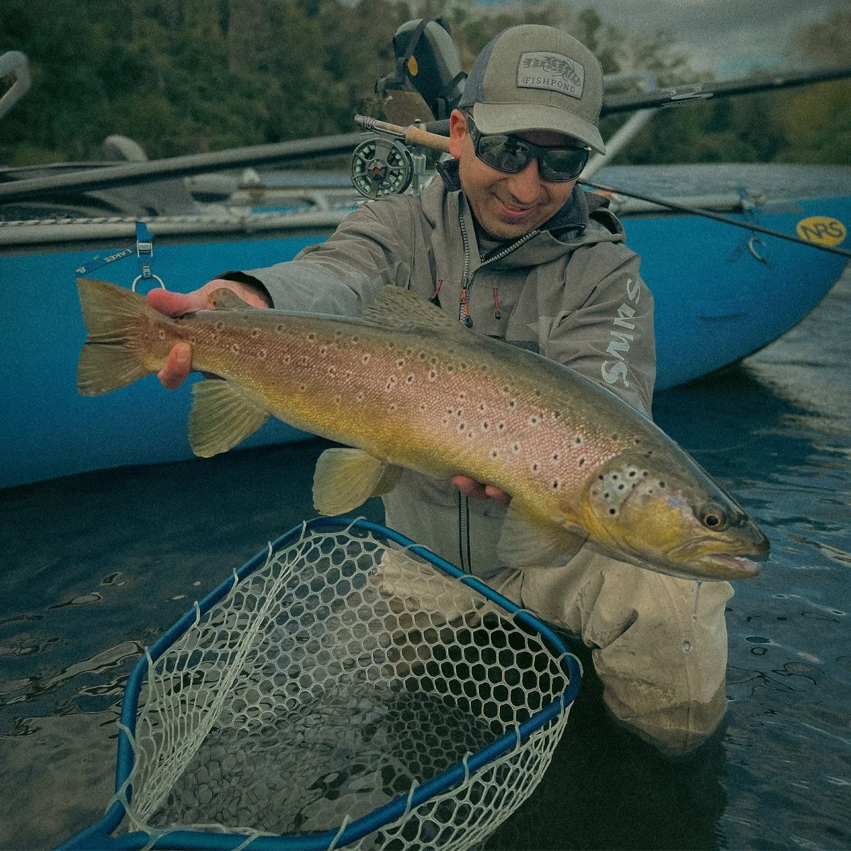 Angler holding a golden wild brown trout beside a drift boat on a private guided float trip in Puyehue, Chile.