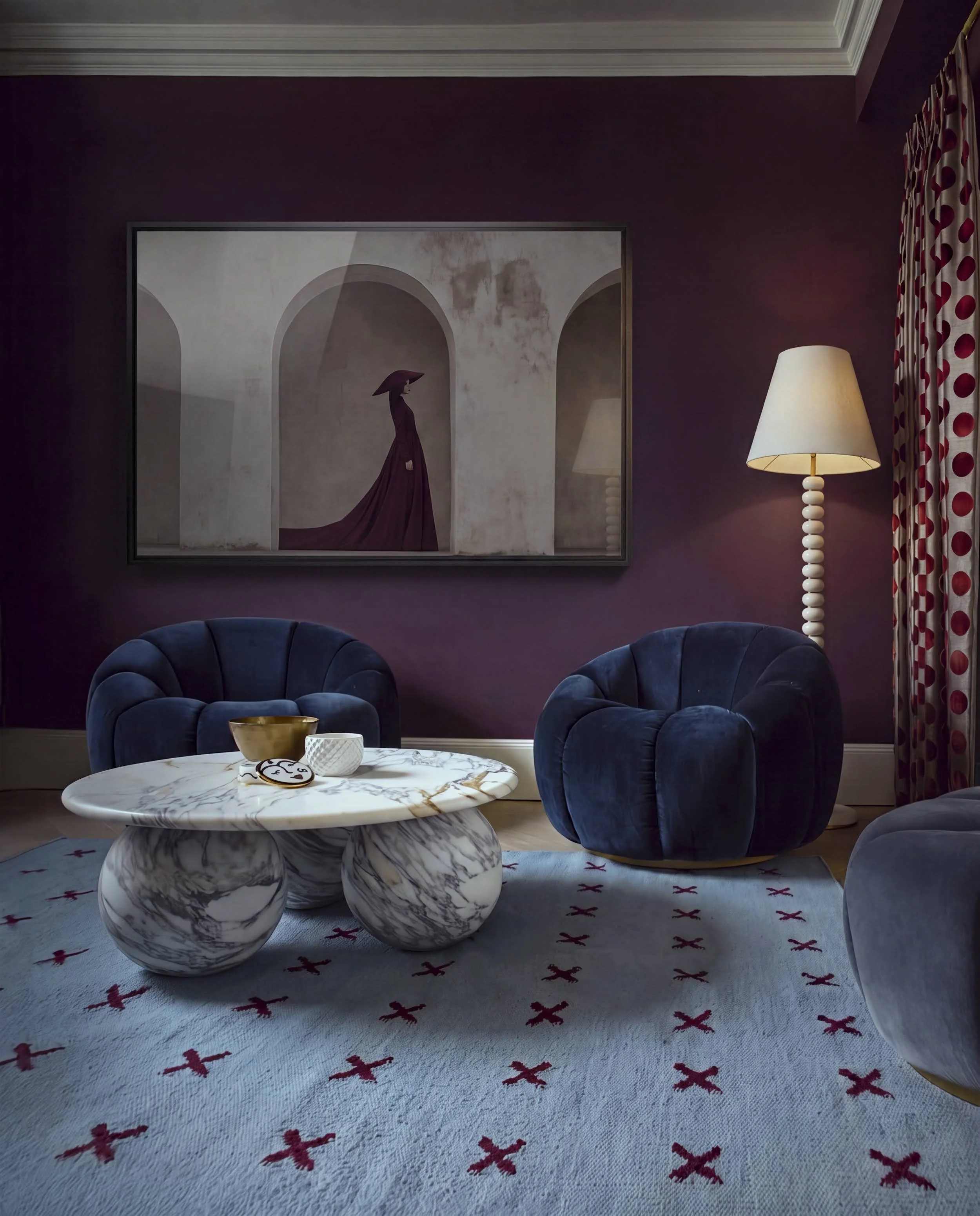 Burgundy sitting room in Notting Hill with navy scalloped velvet armchairs, marble sphere coffee table and cross-motif rug against deep plum walls