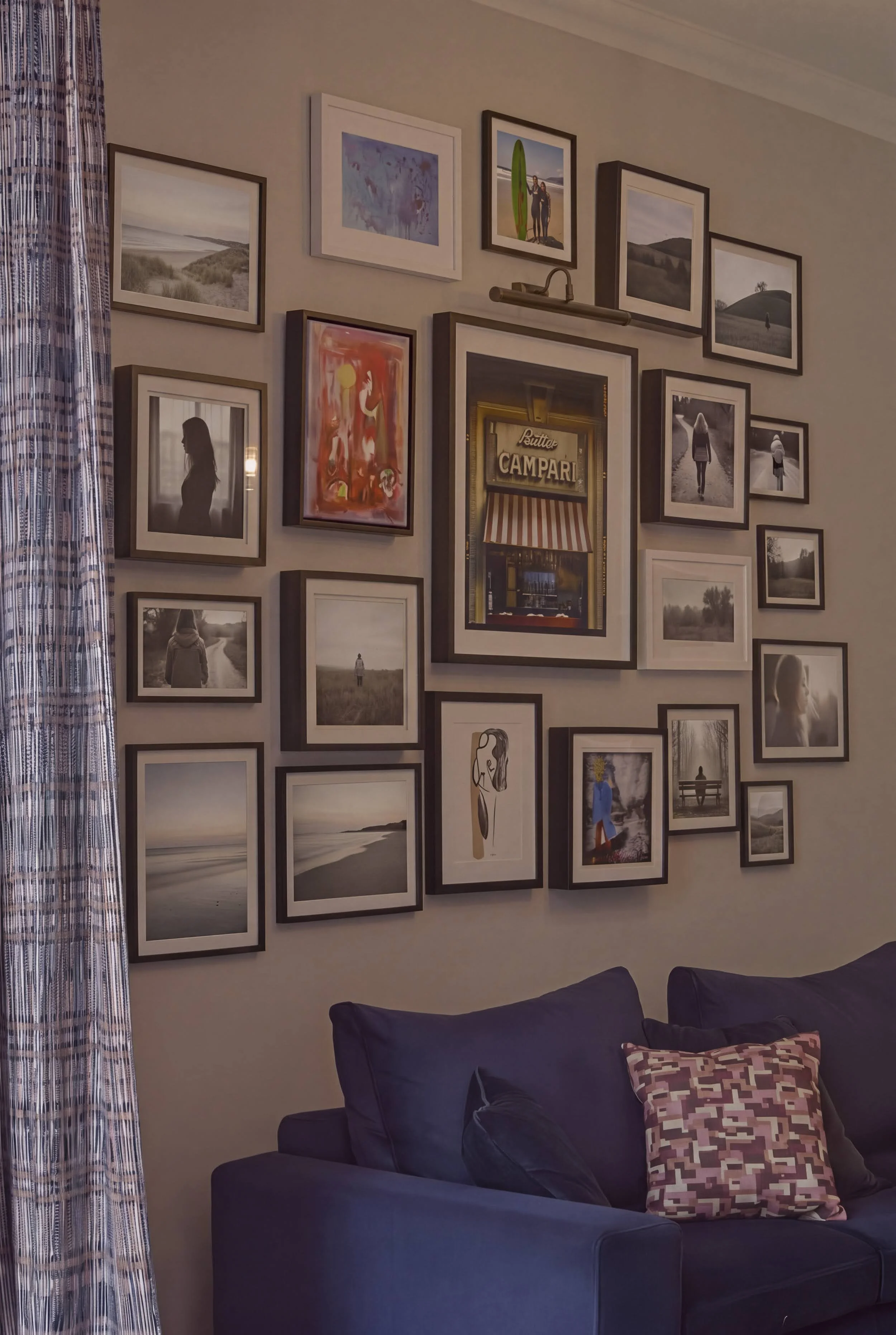 Large curated gallery wall of family photography and art above a navy velvet sofa in a Notting Hill living room