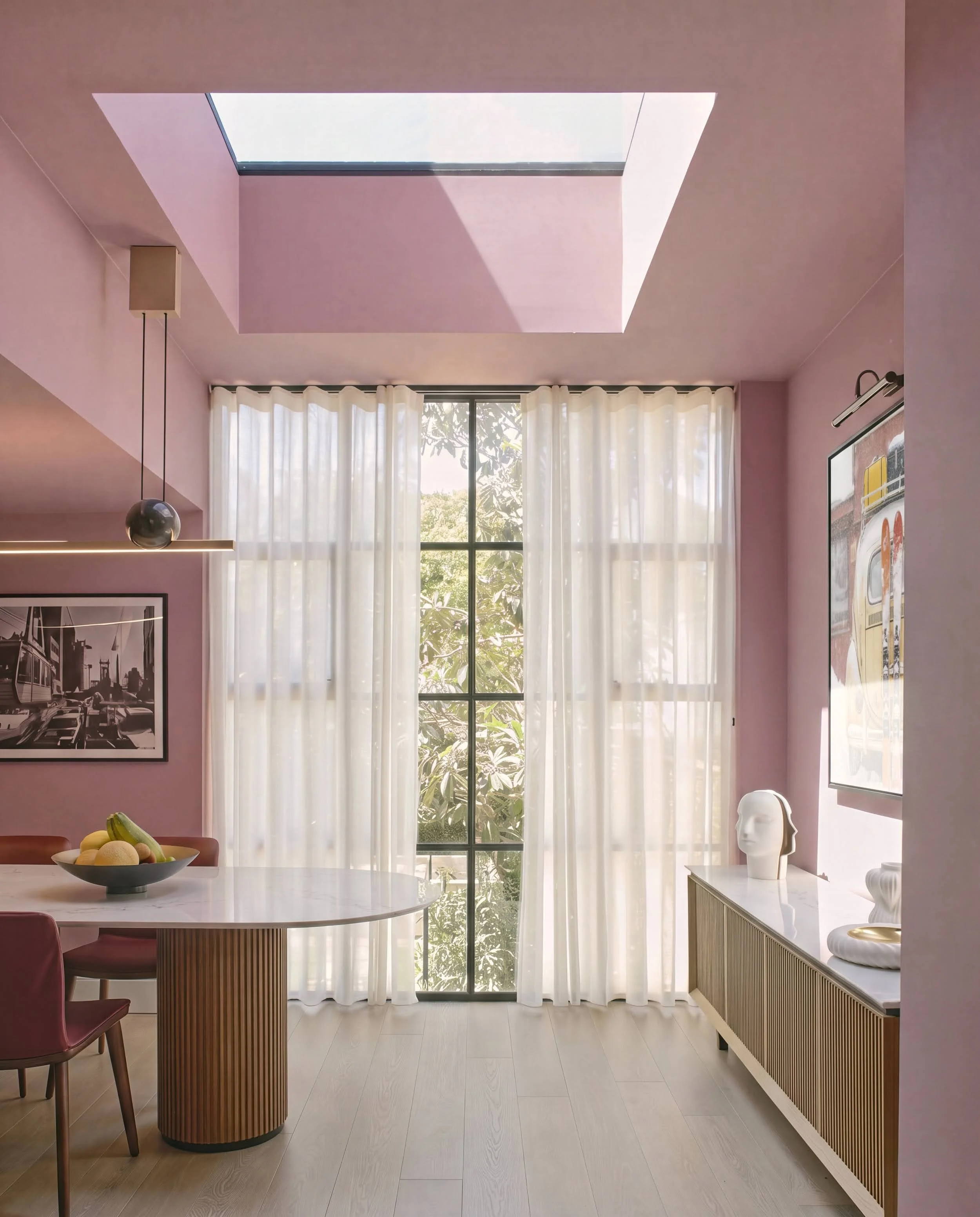 Pink dining room in Notting Hill with rooflight, floor-to-ceiling sheer curtains, fluted oak dining table, and fluted sideboard styled with a plaster head sculpture