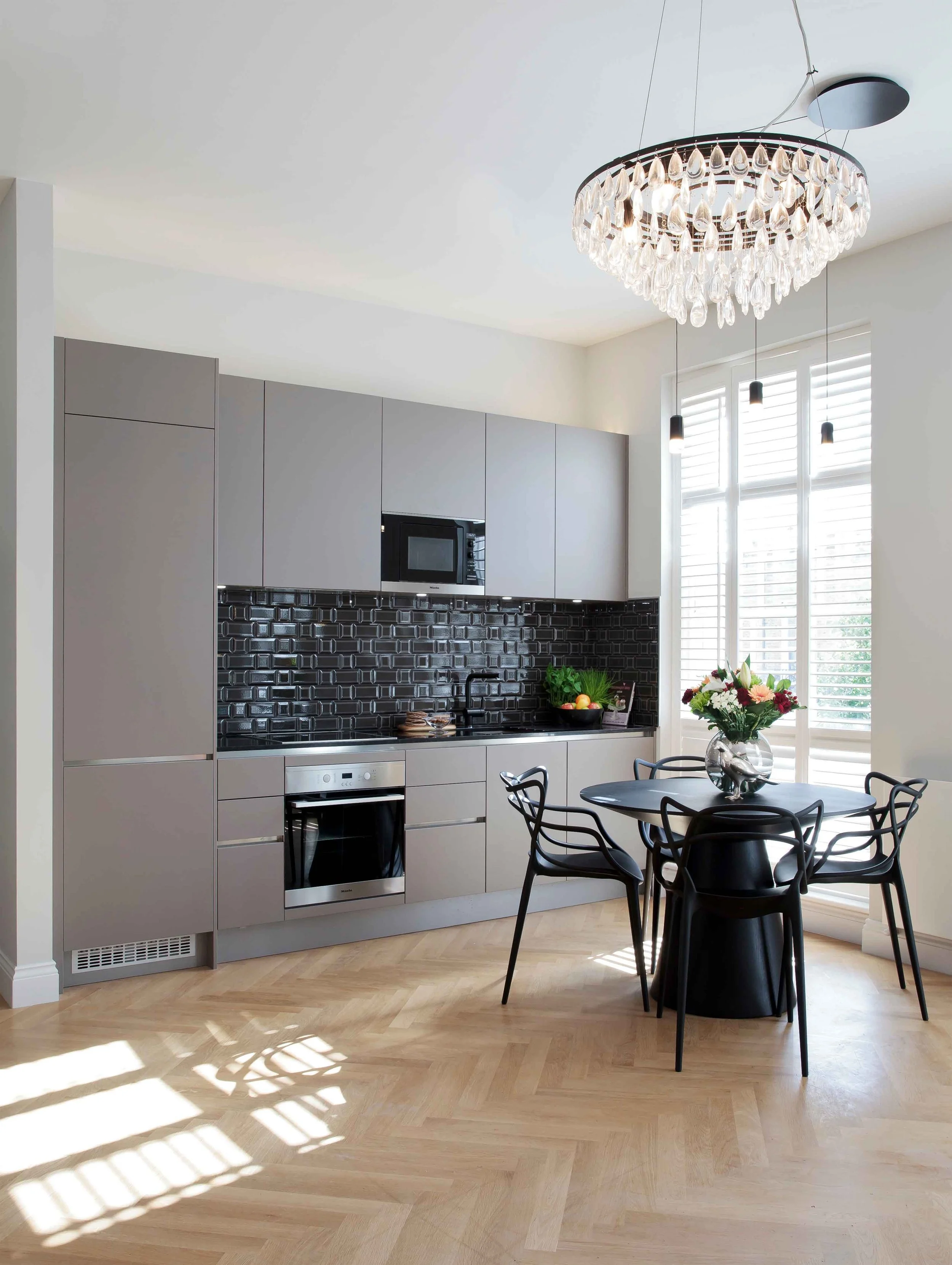 Kitchen with matt grey cabinet, black granite worktop, glossy ceramic splashback tiles, herring bone oak flooring