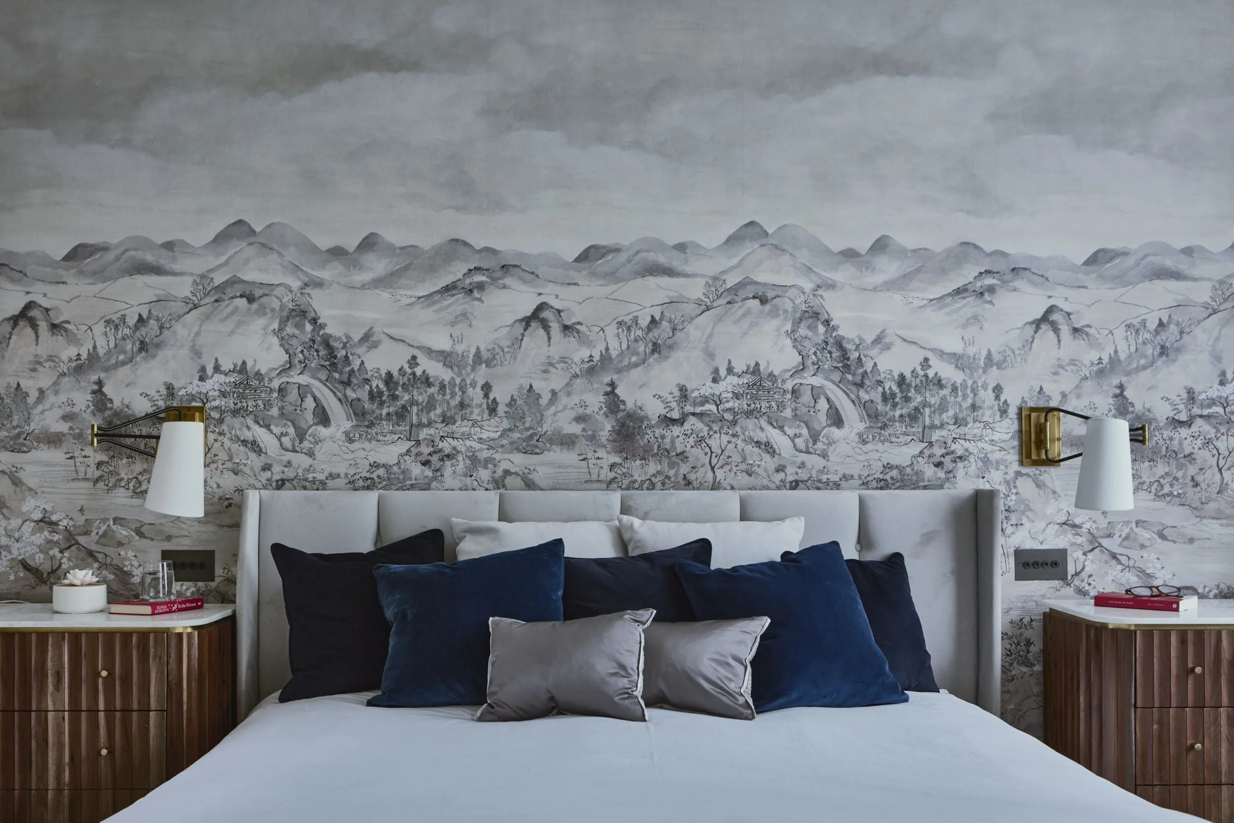 Master bedroom in Notting Hill with Cole & Son mountain landscape wallpaper, upholstered grey headboard, navy velvet cushions and walnut bedside cabinets