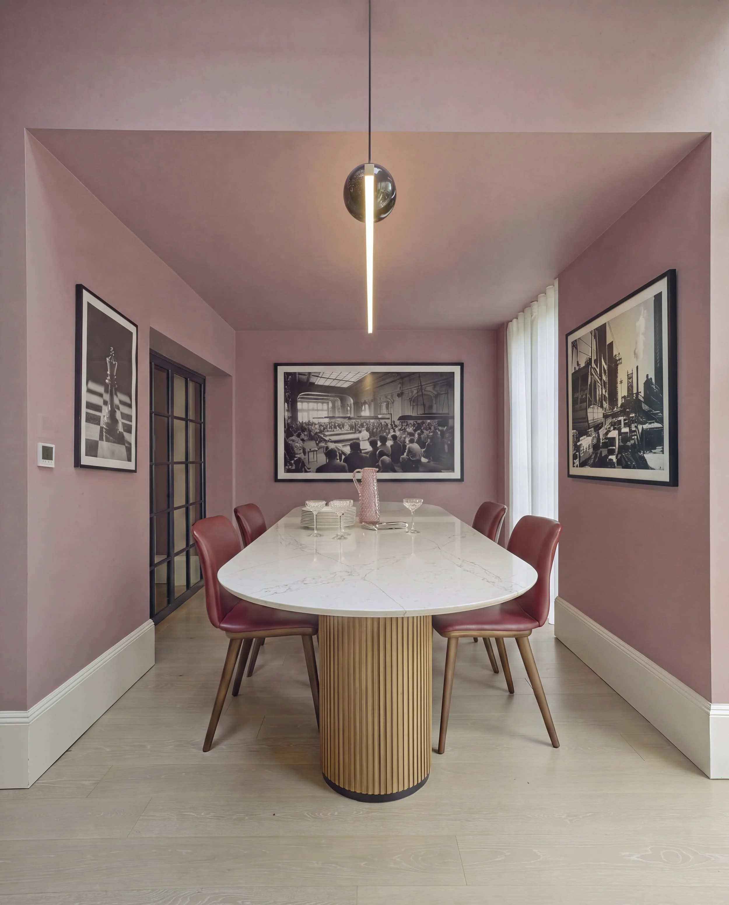 Pink dining room in Notting Hill with marble oval table, fluted oak base, red leather chairs, black-and-white gallery wall and sculptural pendant light