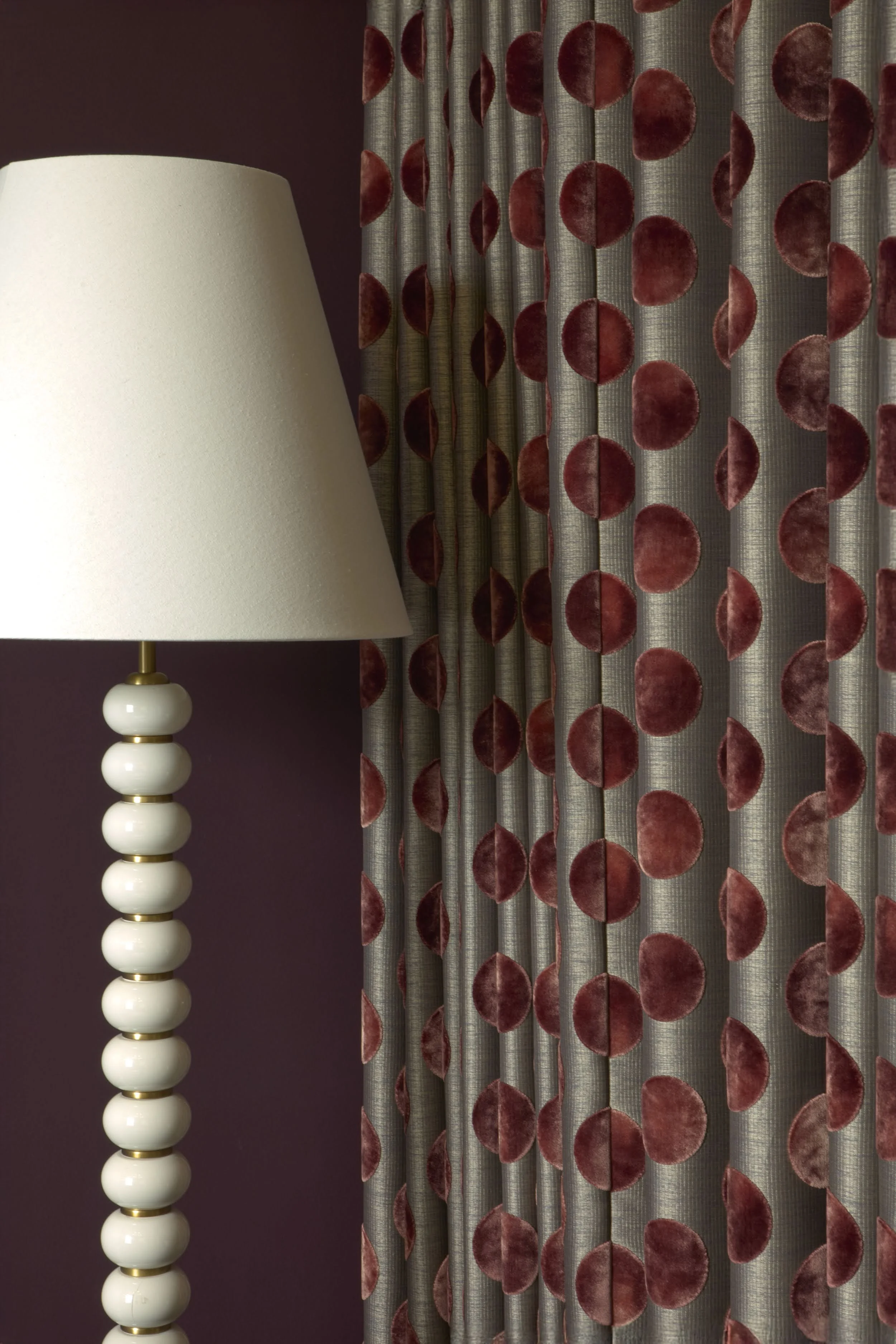 Detail of a stacked ceramic bead floor lamp beside a burgundy polka-dot velvet curtain against a deep plum wall in a Notting Hill living room
