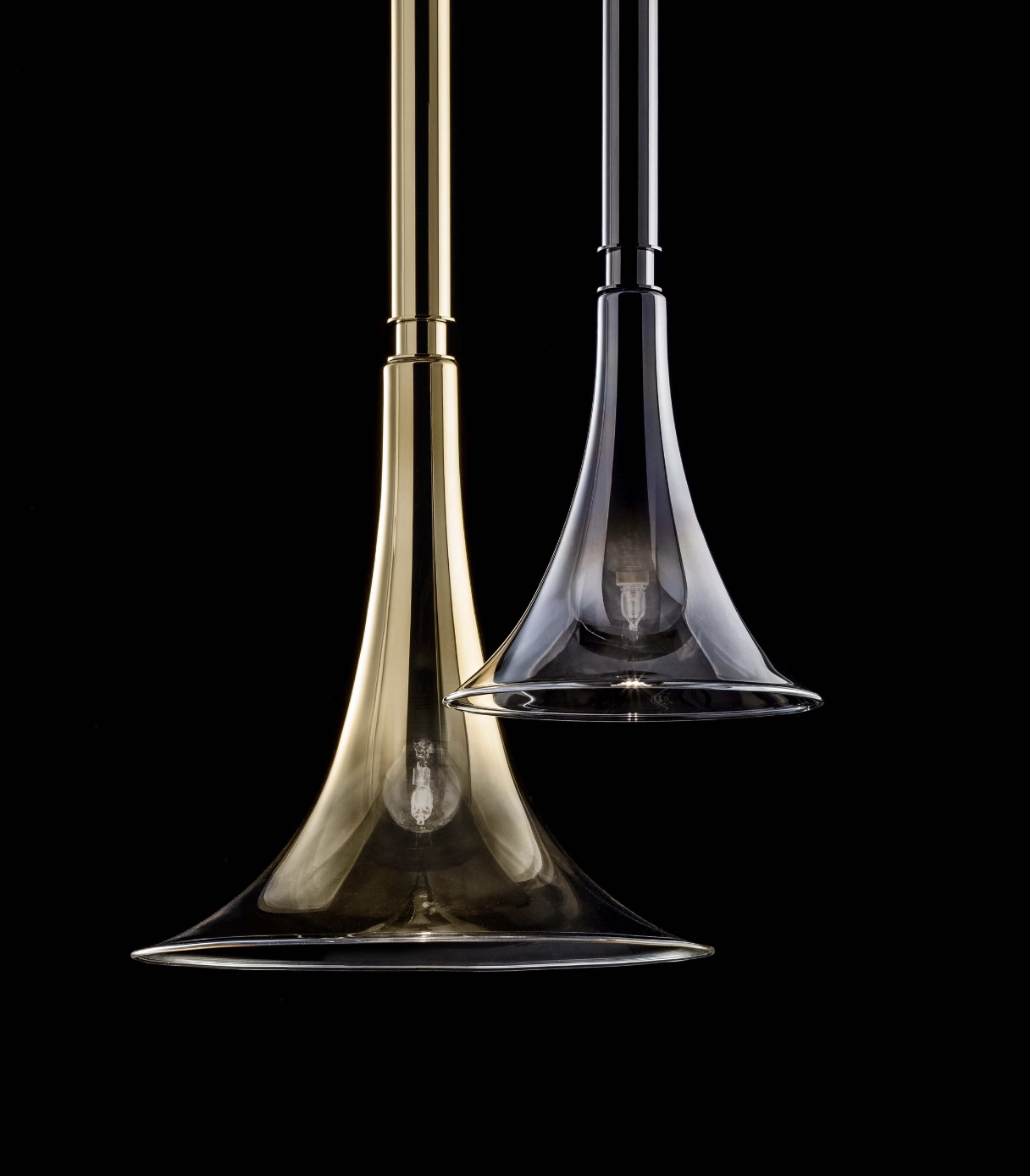 Two modern pendant light fixtures with glass shades, one gold and one black, hanging against a black background.