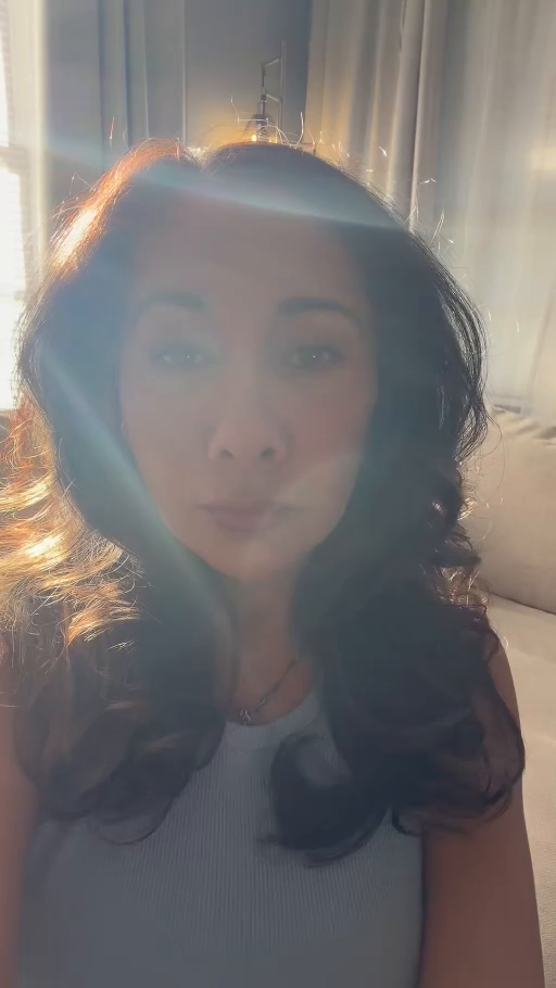 Stephanie facing the camera beside curtains with sunlight and blue-green light crossing the portrait
