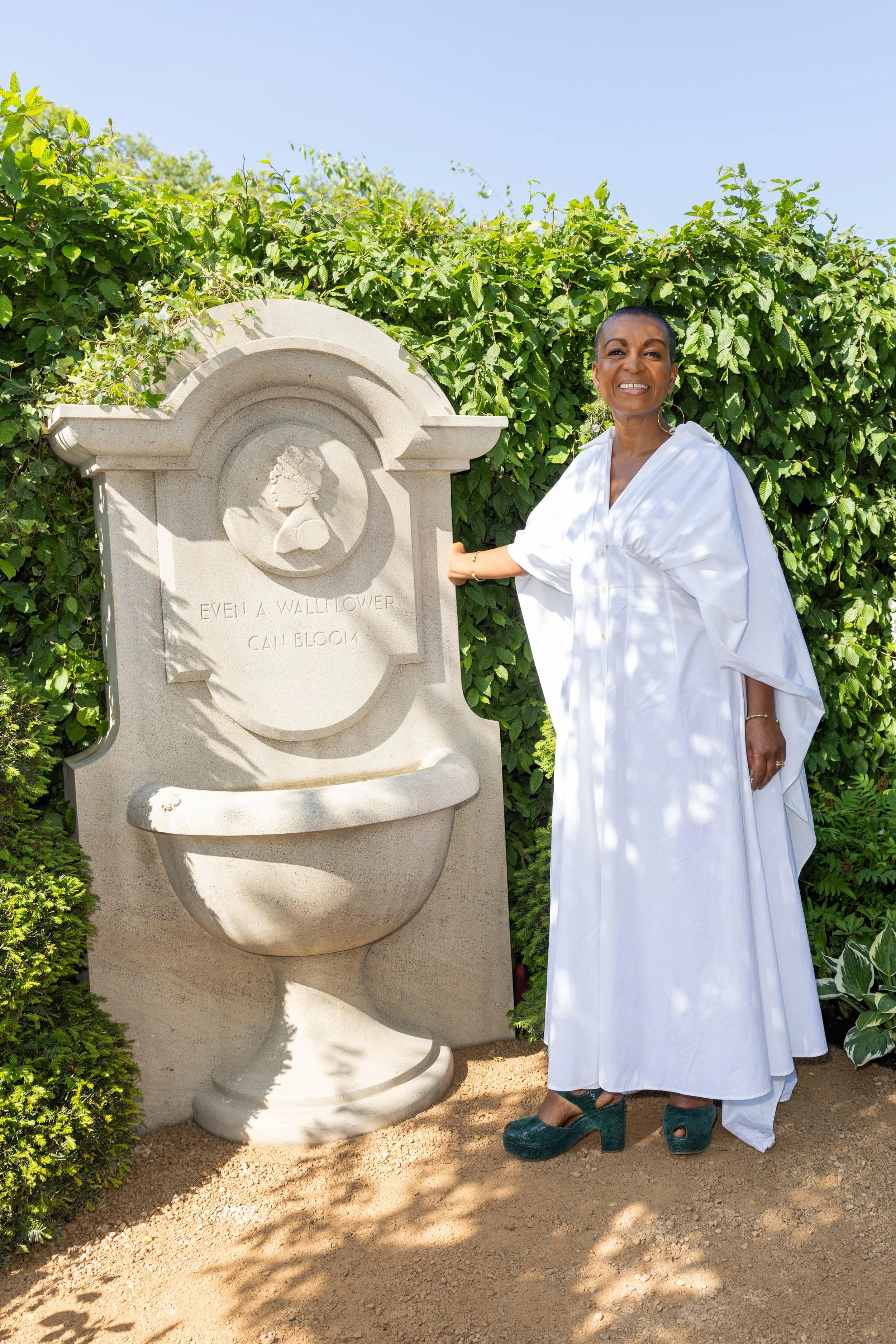 Bridgerton actress Adjoa Andoh stands by the Lady Whistledown sculpture in the Bridgerton Garden.
