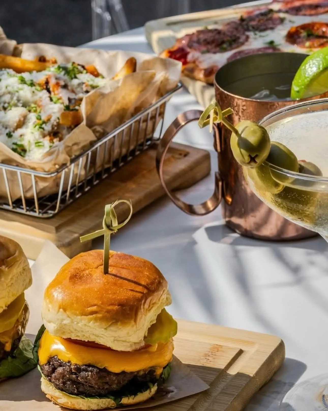 Close-up of a cheeseburger topped with a biscuit, lettuce, tomato, melted cheese, and a beef patty on a wooden board.