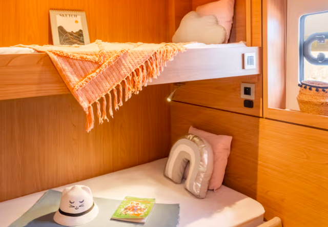 Cozy bunk bed with orange blanket, pillows, hat, and book in a wooden cabin interior.