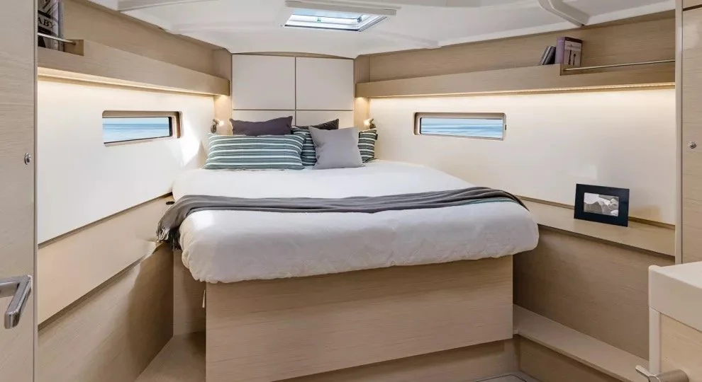 Modern yacht cabin interior with a bed, two windows, striped pillows, and a skylight.