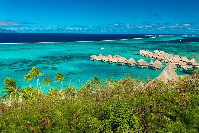 sailing catamaran anchored in french polynesia next to overwater villas