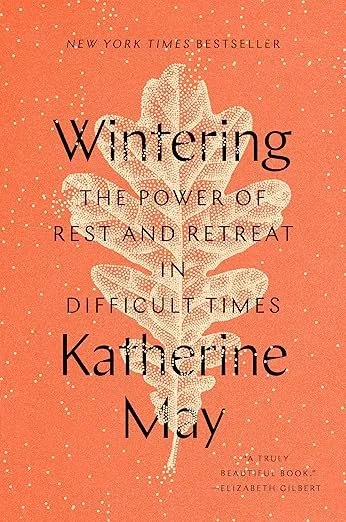 Book cover of 'Wintering: The Power of Rest and Retreat in Difficult Times' by Katherine May, with a white leafy plant illustration on a coral background with gold specks. Book recommendation from a Salt Lake City therapist