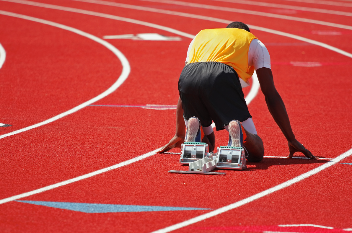 Athlete in starting position on a red running track with starting blocks ready