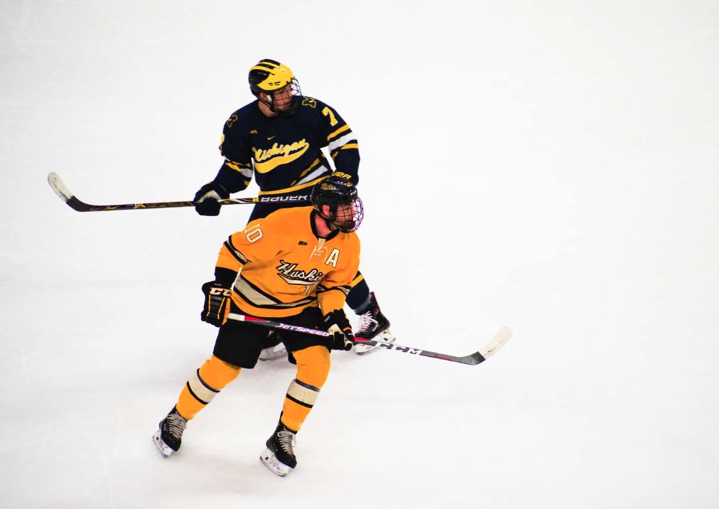 Two ice hockey players, one in yellow and the other in navy blue, compete on the ice rink.