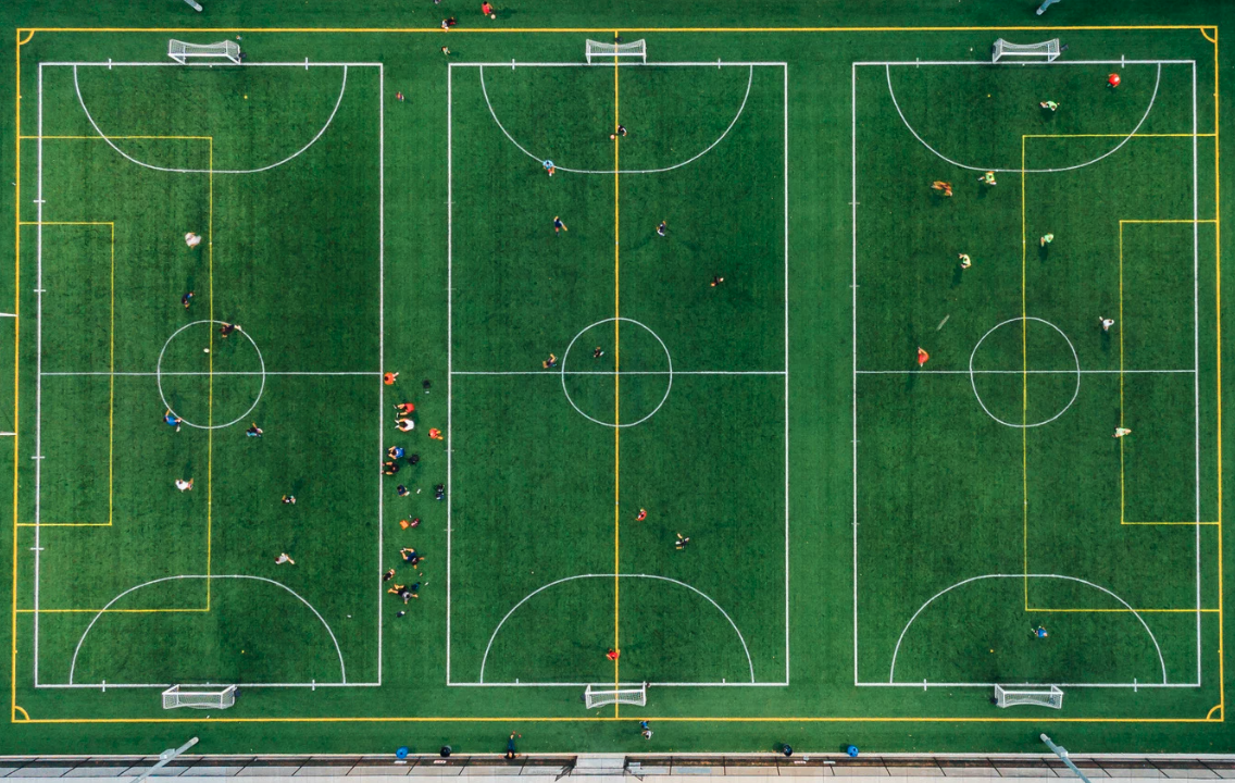 Aerial view of a multi-field soccer complex with three full-sized fields, occupied by players and spectators.