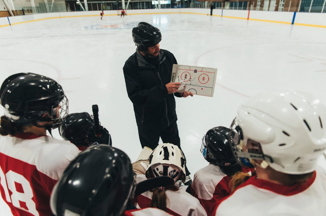 Hockey coach giving instructions to players during practice on an ice rink.