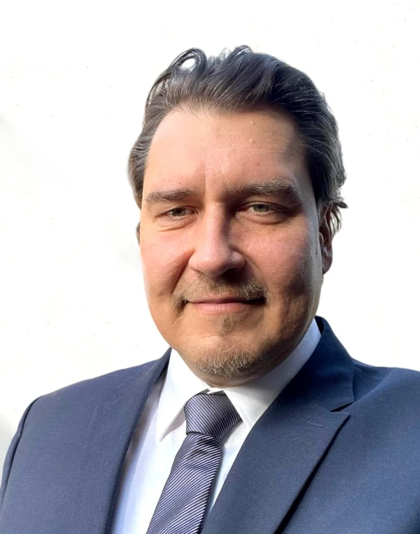 Portrait of a man in a suit and tie against a white background.