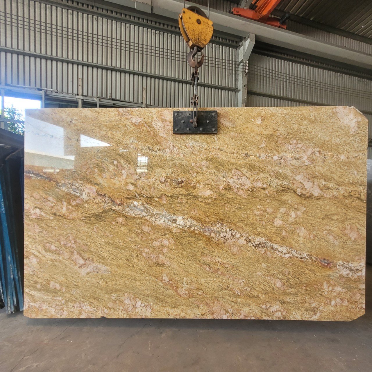 Large granite slab with yellow and pink patterns hanging in a warehouse.