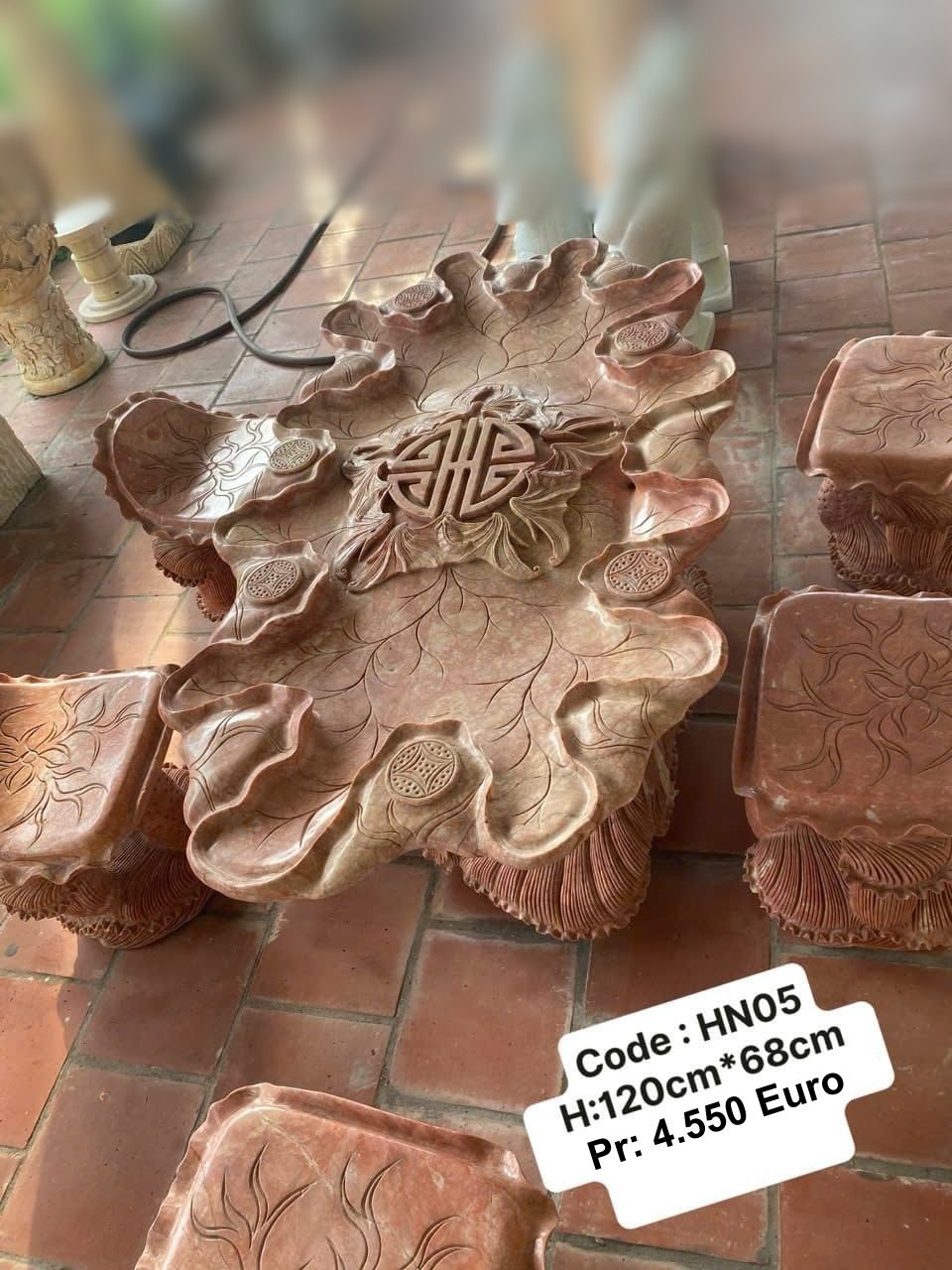 Wooden carved table with floral design and a central Chinese symbol, surrounded by matching wooden stools, on a tiled floor.