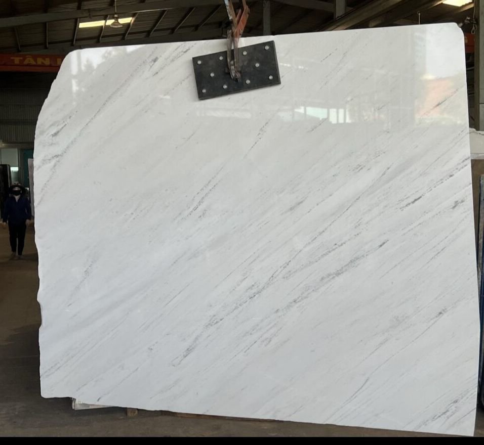 Large white marble slab with gray veining suspended in a warehouse