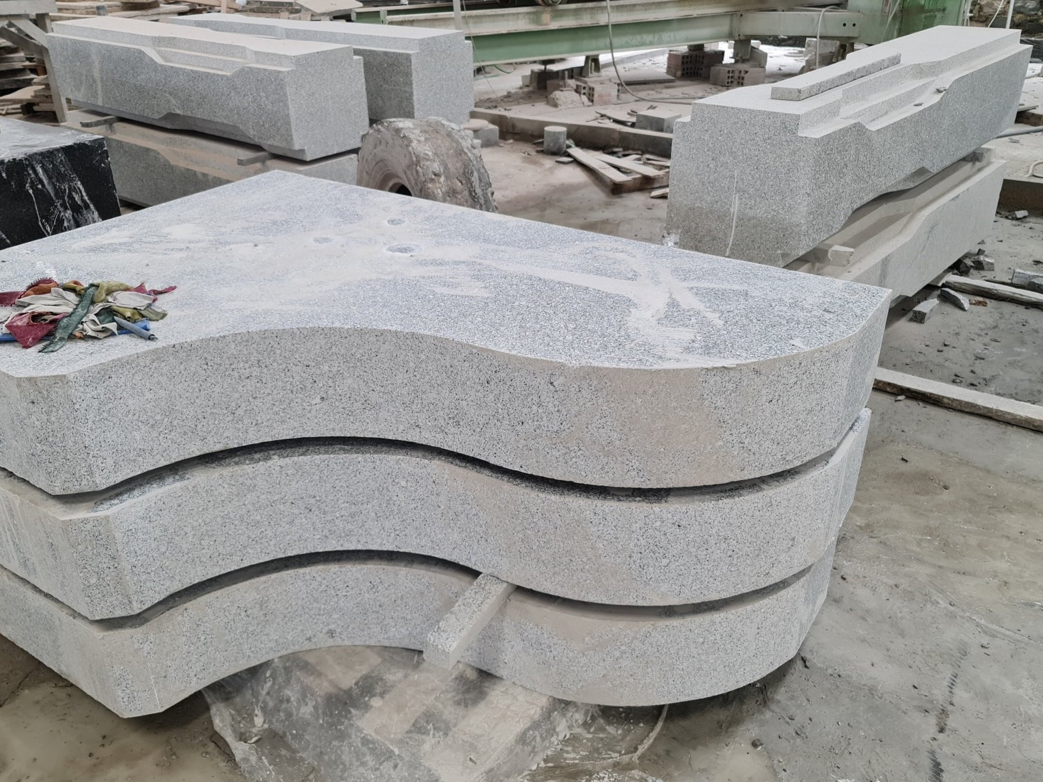 Stack of large cut stone slabs in a workshop with machinery and tools visible in the background.