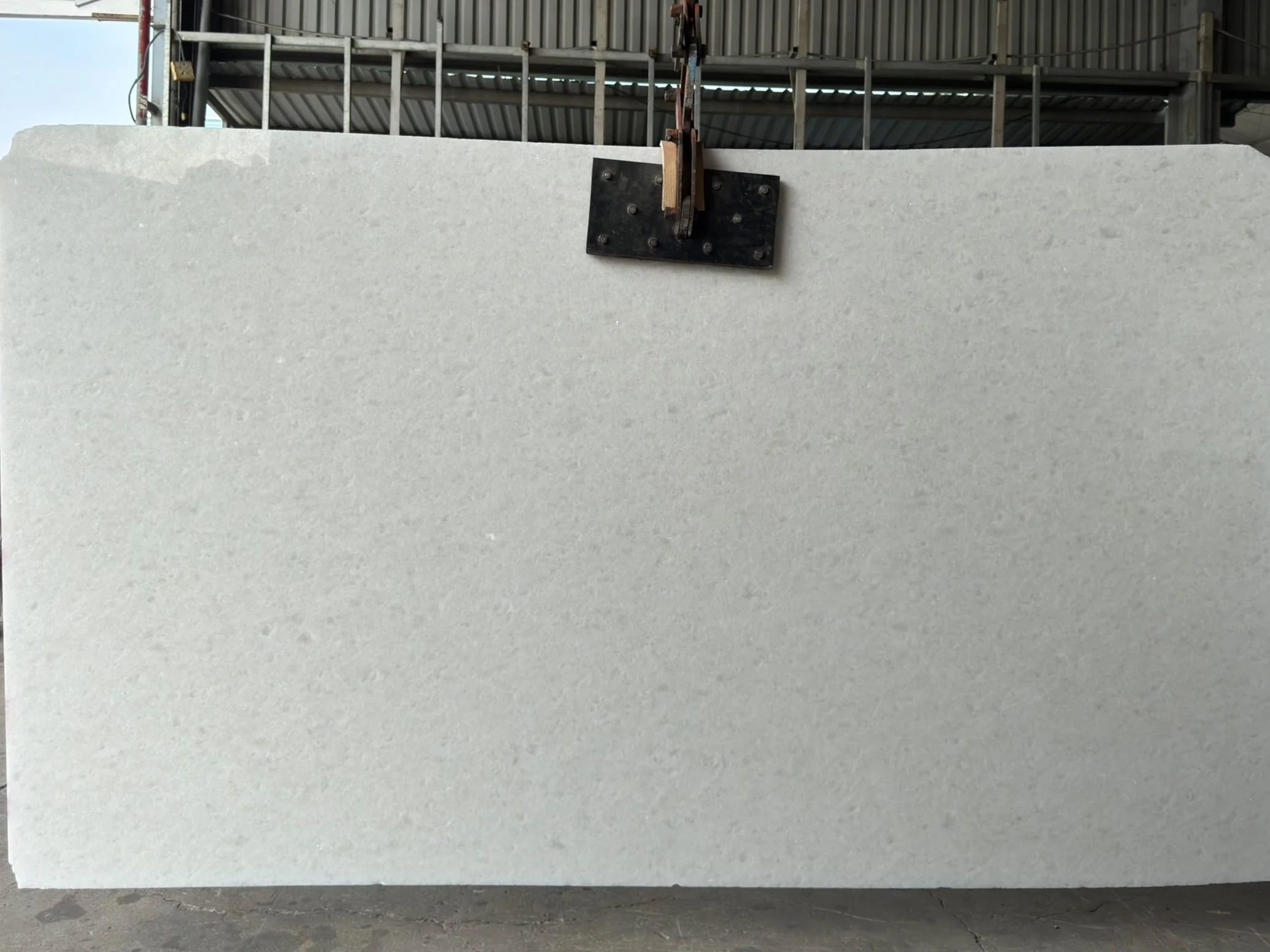 Large white marble slab suspended by a clamp in an industrial setting