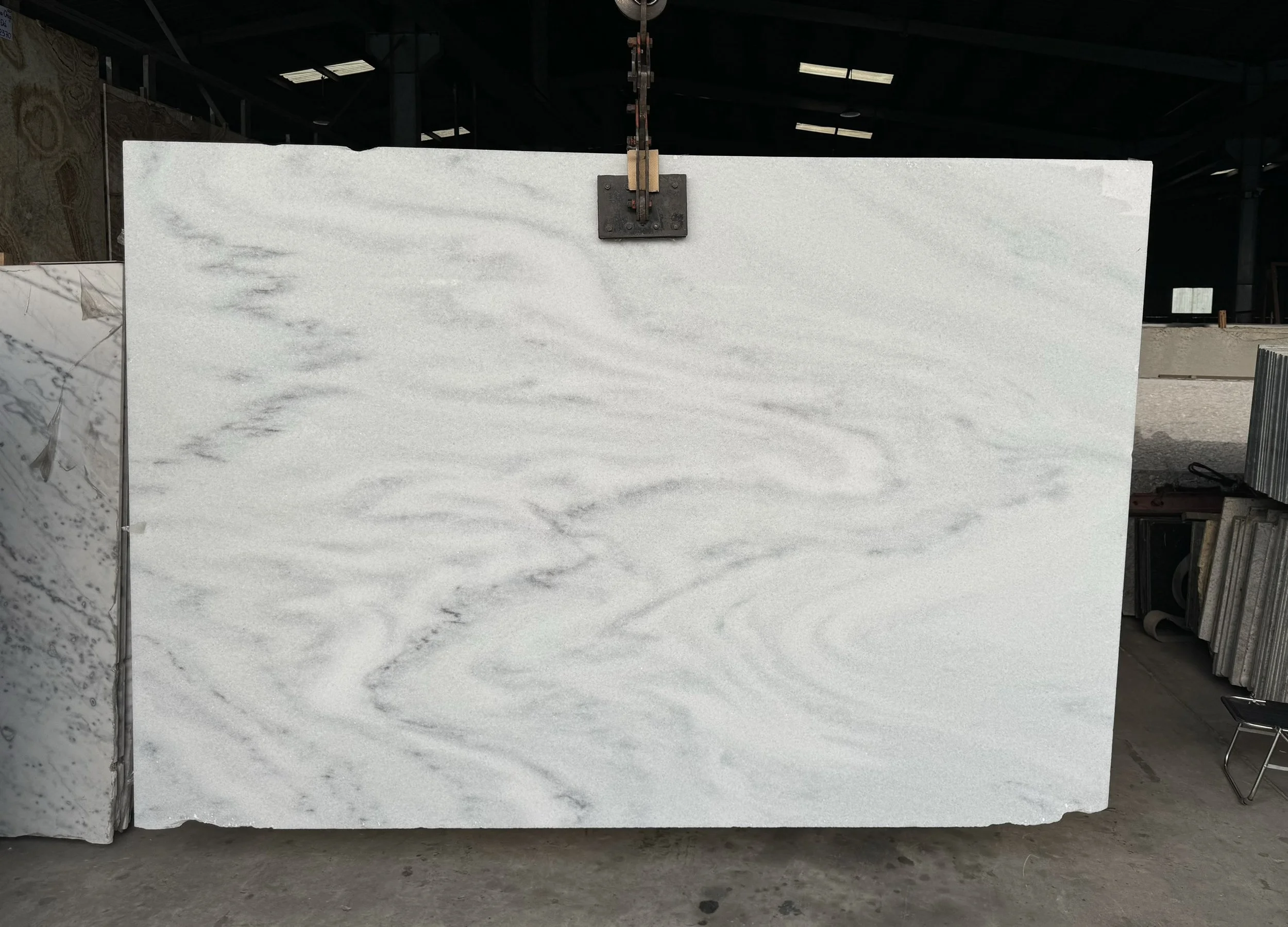 Large white marble slab with subtle gray veining in a warehouse setting.