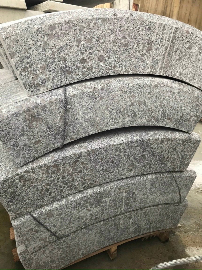 Stack of curved granite slabs on a wooden pallet, arranged in an orderly manner.