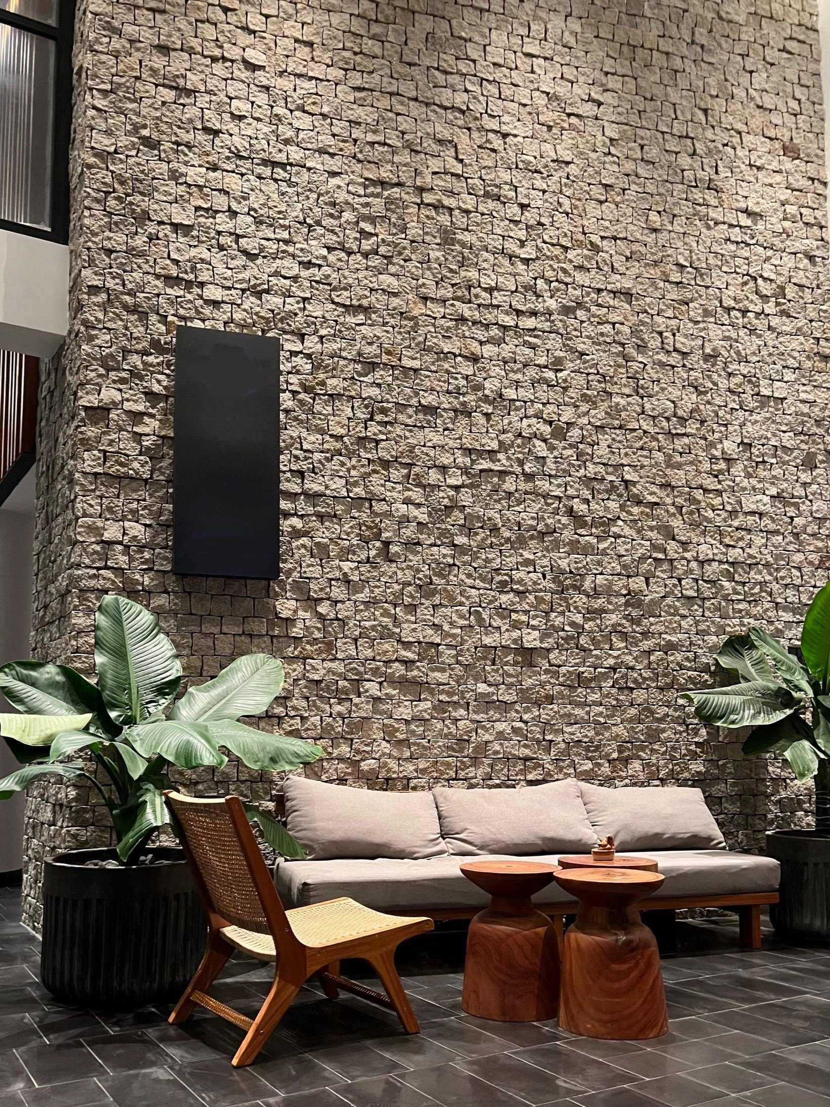 modern interior with stone feature wall, sofa, wooden chair, potted plants, and coffee table