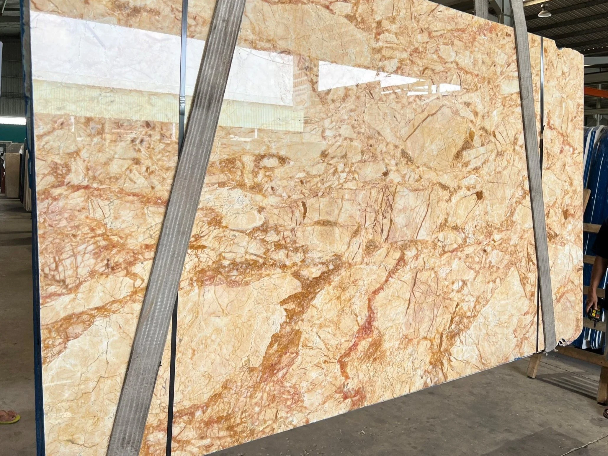 Large marble slab with beige and brown veining in a warehouse