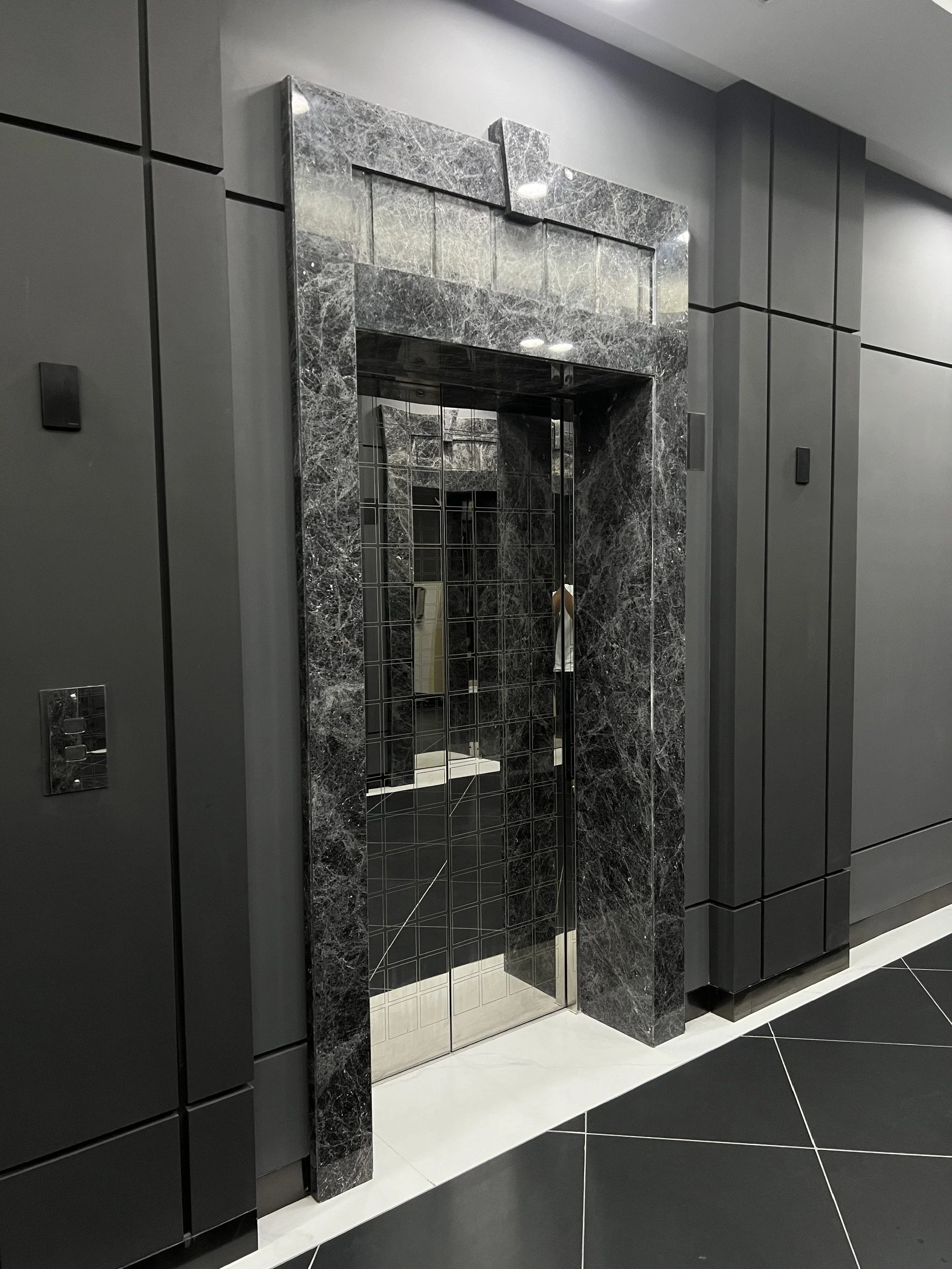 Modern elevator entrance with marble frame and reflective doors in a sleek building interior.