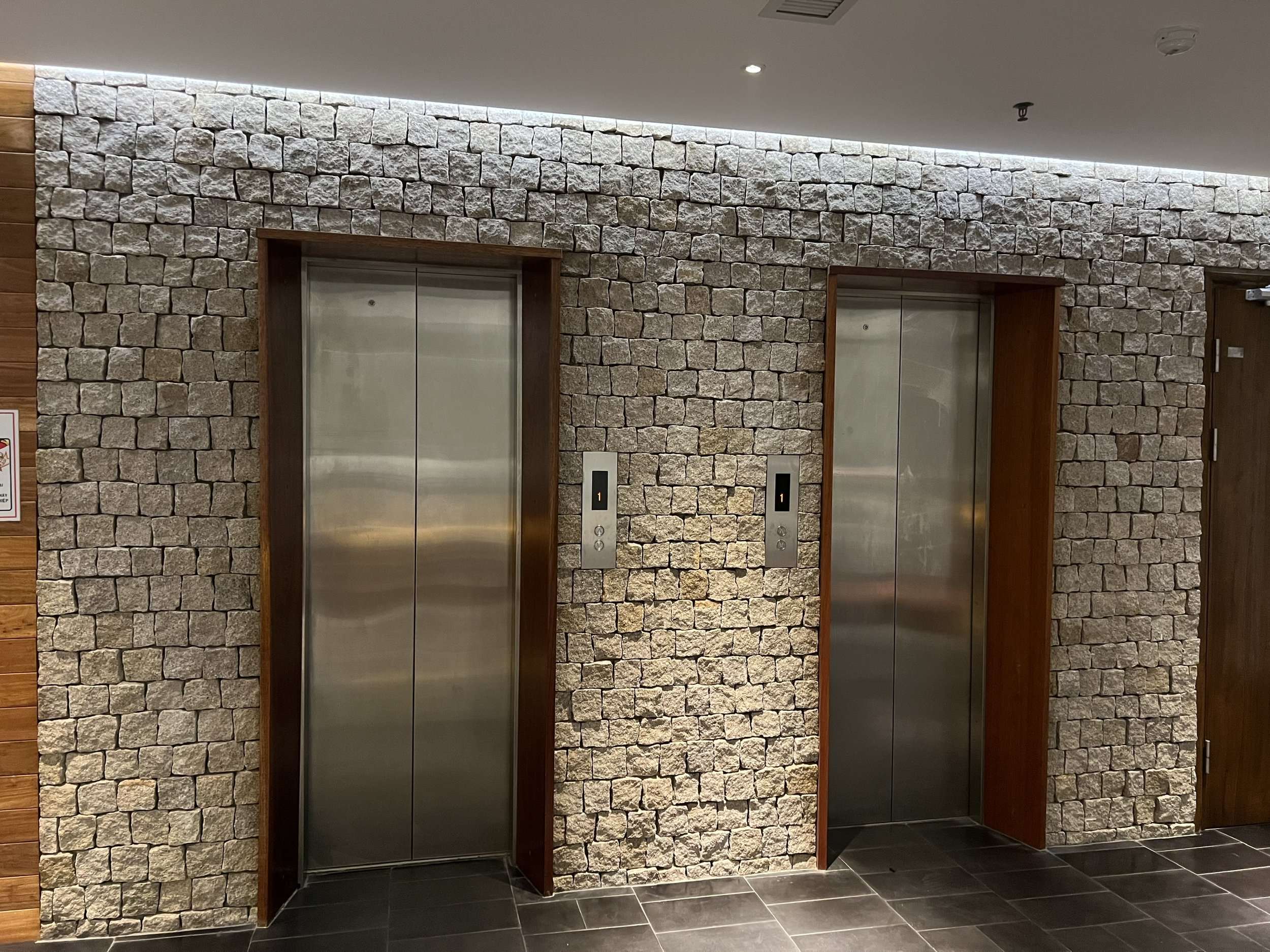 two elevators in modern lobby with stone wall and tile floor