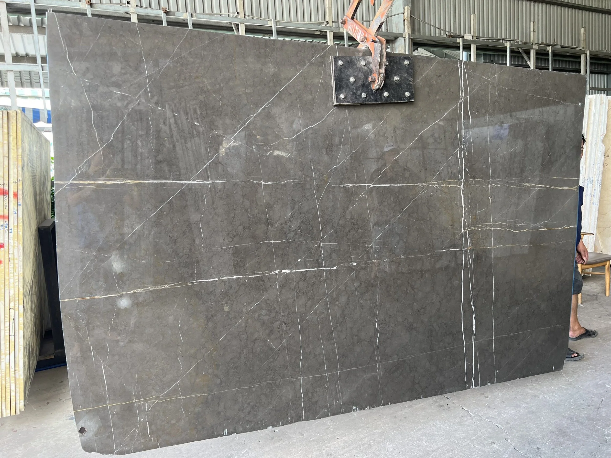 Large dark gray marble slab with white veining in a warehouse setting