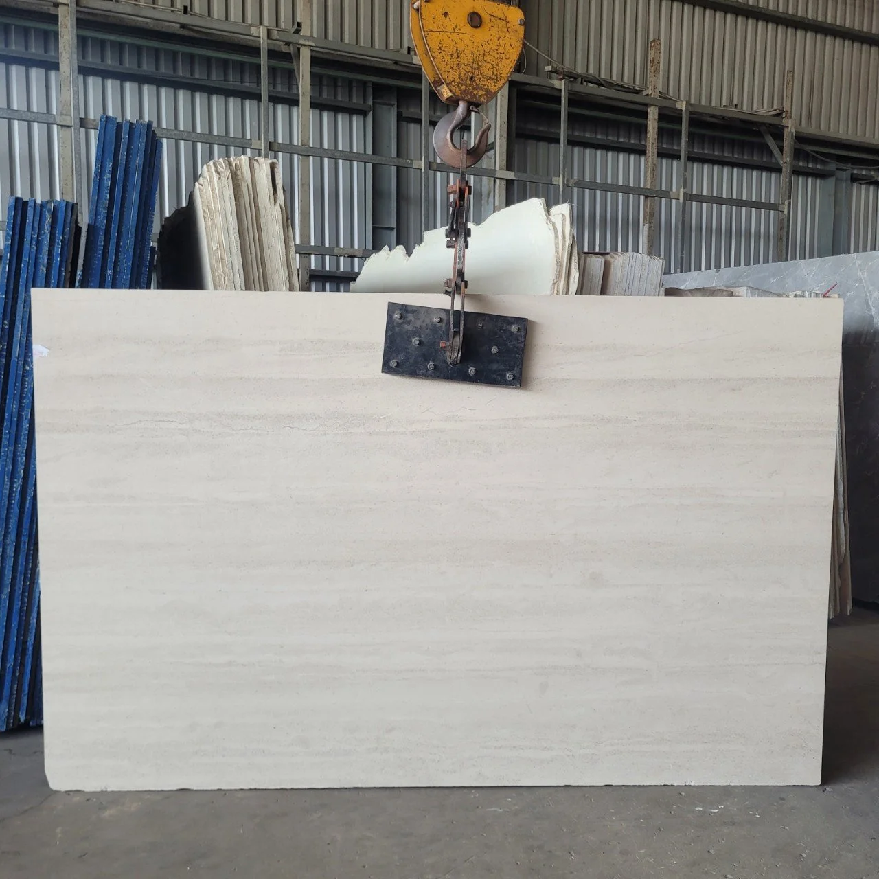 Large stone slab suspended by an industrial crane in a warehouse