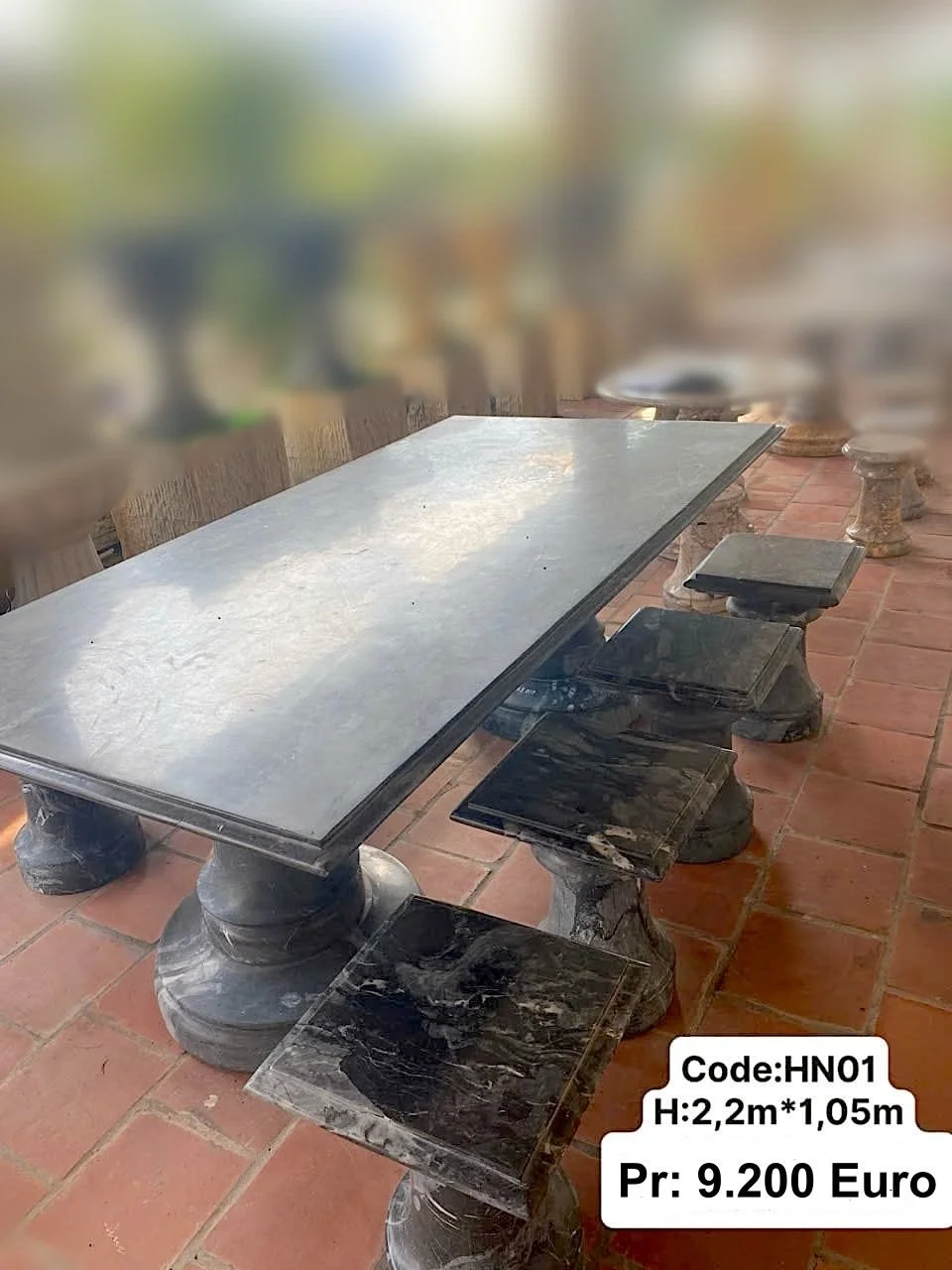 A long rectangular marble dining table with a light grey top and black marble-styled legs, accompanied by black marble-styled benches with matching bases, set on a red brick floor.