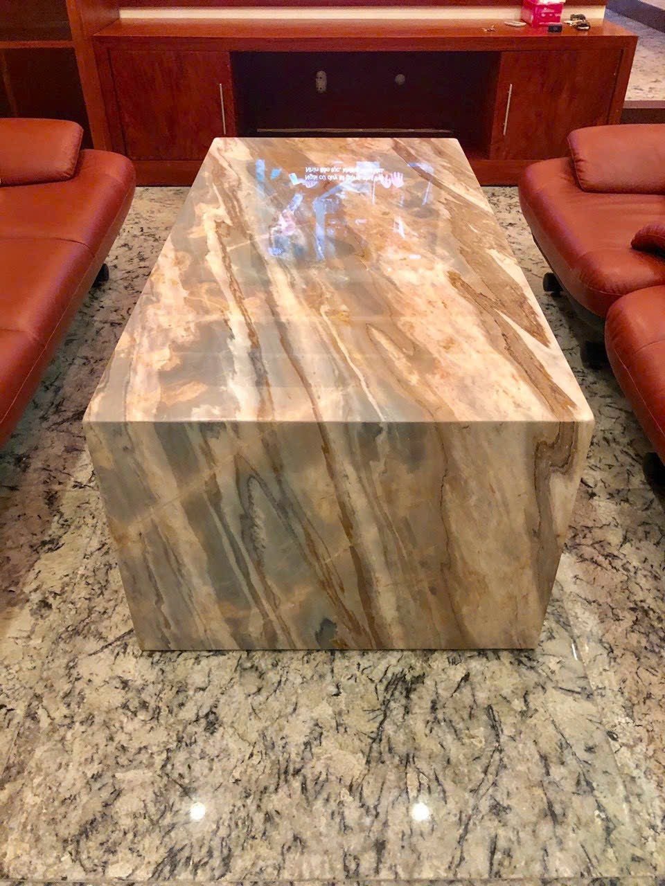 Marble coffee table on speckled stone floor with brown sofas and wooden cabinet in the background.